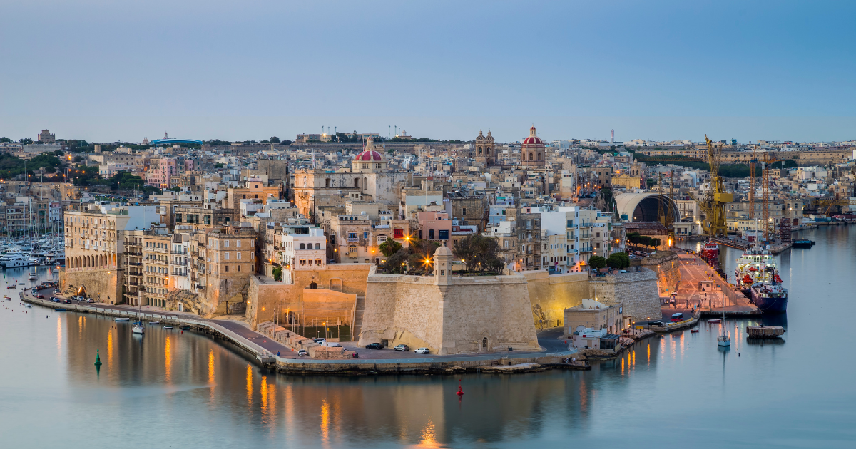 Panoramic view of Malta’s Grand Harbour, featuring historic fortifications, waterfront buildings and maritime infrastructure at dusk.